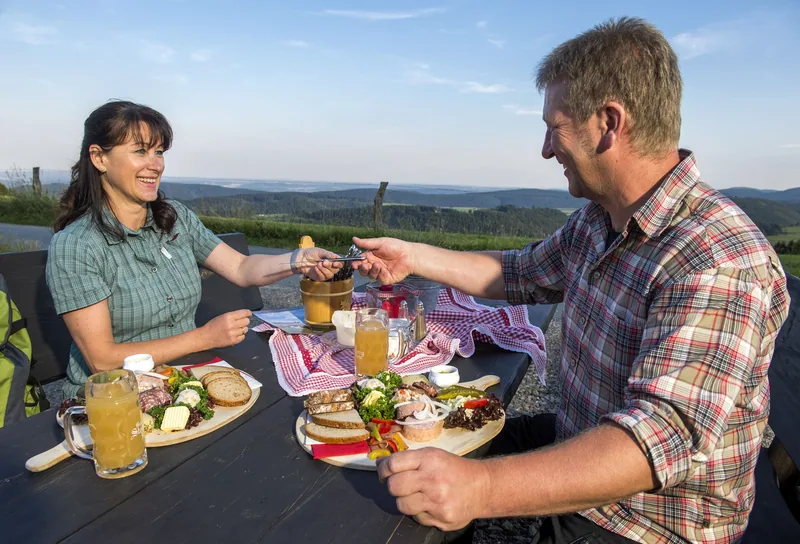 Wanderpaar bei der Brotzeit auf einer Hüttenterrasse mit Weitblick