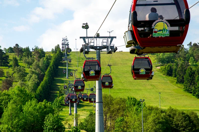 Rode gondels van de Ettelsberg-gondelbaan boven groene hellingen