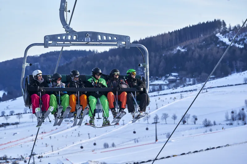 Sechs Skifahrer auf einer Sesselbahn über verschneiten Hängen